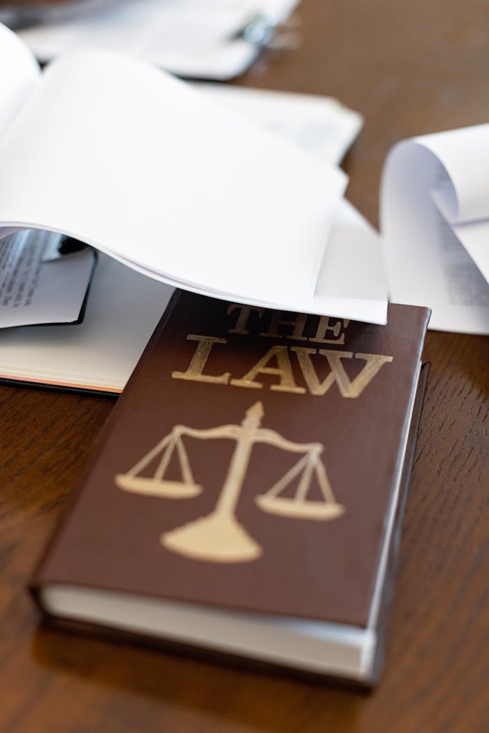 Close-up of a law book with scales icon on a wooden desk covered in papers.